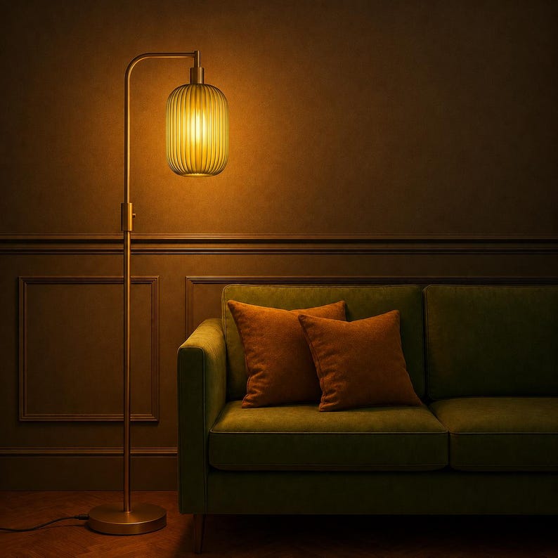 May include: A tall floor lamp with a slender metallic stand and a cylindrical, vertically ribbed glass shade emitting a warm, golden light. The lamp features a circular base and a curved arm that supports the glowing, textured glass light fixture.