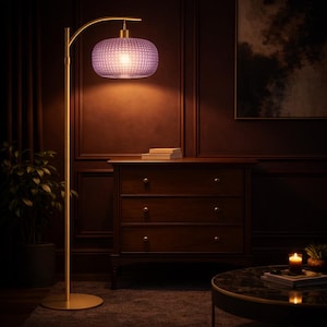 May include: A gold-colored floor lamp with a curved arm and a purple, textured lampshade. The lamp is in a room with dark wood paneling, a wooden dresser, and a round coffee table. A small plant is visible.