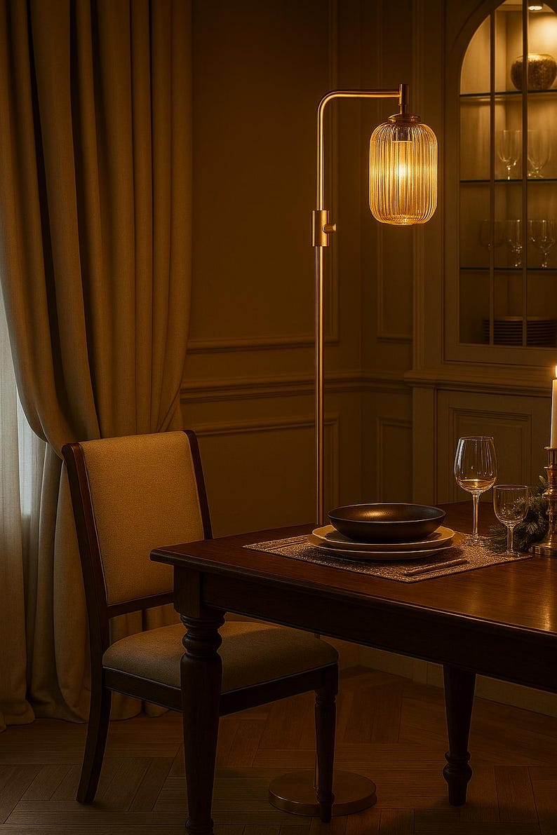 May include: A tall floor lamp with a slender metallic stand and a cylindrical, vertically ribbed glass shade that emits a warm glow. The lamp is positioned next to a wooden dining table set with stacked plates, a bowl, and glassware.