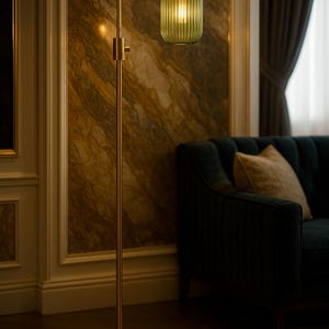 May include: A floor lamp with a slender brass-toned metal stand and a circular base. The lamp features a single downward-facing light source enclosed by a cylindrical, vertically ribbed, translucent olive green glass shade with a brass cap.