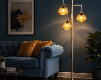 May include: A tall floor lamp with a slender brass-finished metal stand and a circular base. The lamp features three hanging lights with round, textured amber glass shades that emit a warm, glowing light, arranged at varying heights.