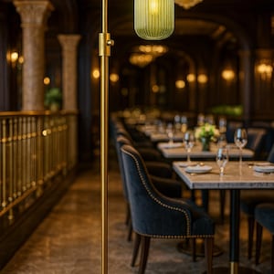 May include: A floor lamp with a tall, slender brass-colored metal stand and a circular base. The lamp features a single, vertically ribbed, translucent green glass shade that hangs downward from a curved arm, emitting a warm, soft light.