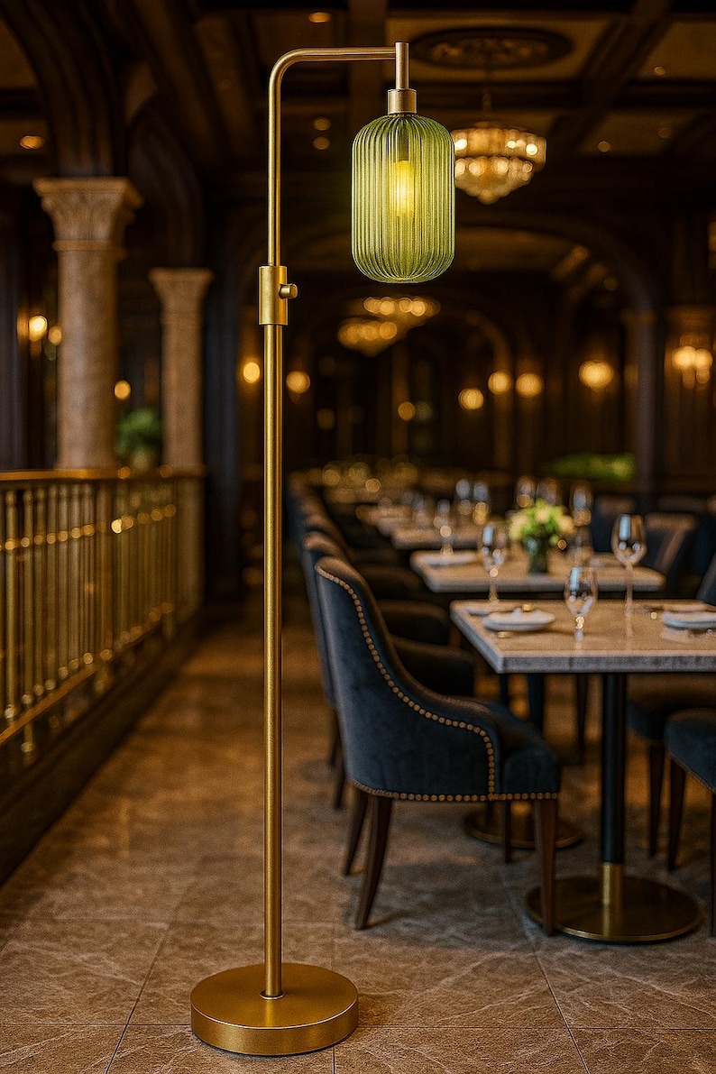 May include: A floor lamp with a tall, slender brass-colored metal stand and a circular base. The lamp features a single, vertically ribbed, translucent green glass shade that hangs downward from a curved arm, emitting a warm, soft light.