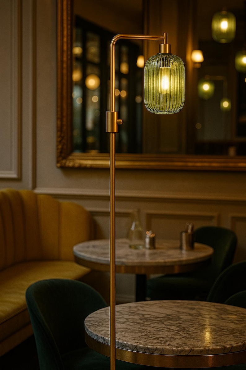 May include: A floor lamp with a slender, matte gold metal stand and a single, vertically ribbed, translucent green glass shade. The lamp features a simple cylindrical design with a warm, glowing light bulb visible inside the glass fixture.