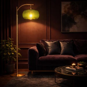 May include: A gold floor lamp with a textured green glass shade illuminates a living room. The lamp is positioned near a dark purple velvet sofa with black leather pillows. A round coffee table and a potted plant are also visible.