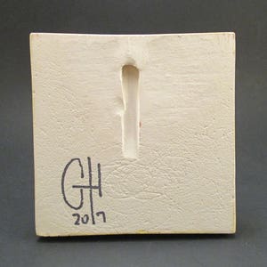 May include: White ceramic tile with a rectangular hole in the centre. The tile is signed "GH 2017" in black marker.