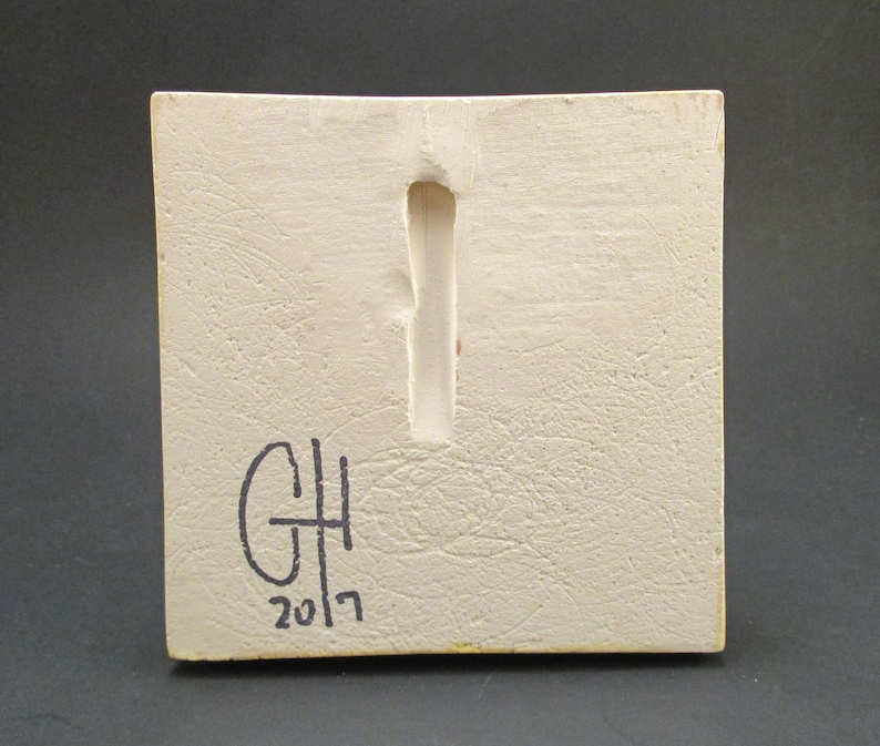 May include: White ceramic tile with a rectangular hole in the centre. The tile is signed "GH 2017" in black marker.