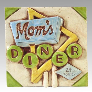 Könnte beinhalten: Eine Keramikfliese mit einem 3D-Design eines Diner-Schilds. Das Schild ist blau und gelb mit den Worten "Mom's Diner" in braunen Buchstaben. Die Fliese hat auch einen grünen und gelben Rand und ein kleines blaues Schild mit der Aufschrift "24 Stunden".