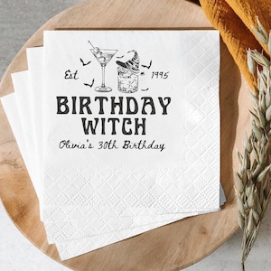 May include: White paper napkins with a diamond pattern and the text "BIRTHDAY WITCH" in bold black letters. The napkins also feature a cocktail glass, a witch's hat, and the text "Olivia's 30th Birthday."