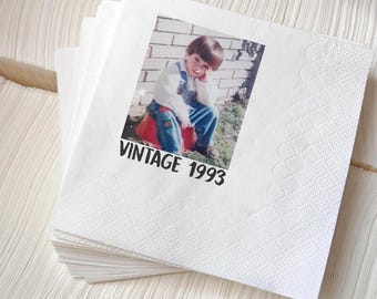 May include: A stack of white paper napkins with a decorative edge. Each napkin features a printed photograph of a child with the text "VINTAGE 1993" in black.