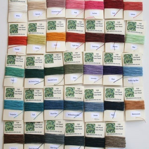 May include: A collection of 4-ply Irish waxed linen thread spools in various colors, including white, natural, Victorian rose, pink, fuchsia, red, salmon, orange, yellow, gold, light rust, dark rust, maroon, mint, sage, dark forest green, emerald green, olive, lavender, plum, robin's egg blue, turquoise, teal, royal blue, Williamsburg blue, denim, navy, butterscotch, walnut, dark chocolate, slate grey, charcoal grey, black, and un-dyed natural. Each spool is labeled with the color name and "4-ply Irish Waxed Linen Thread".