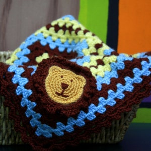 May include: A brown, blue, and yellow crocheted blanket with a brown crocheted bear applique in a wicker basket.