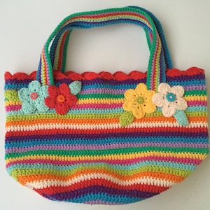 Puede incluir: Una bolsa de mano de crochet a rayas de colores con un borde festoneado y adornos florales. La bolsa tiene un arco&iacute;ris de colores, incluyendo rojo, naranja, amarillo, verde, azul, morado y rosa.