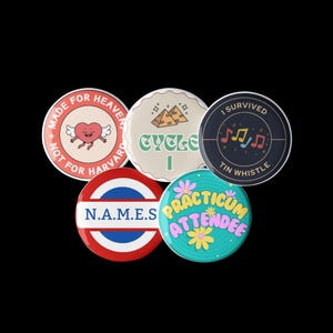 May include: Five colorful round buttons with different designs and text. The buttons feature a heart with wings, a musical note, a pyramid, a circle with the text "N.A.M.E.S", and a flower with the text "PRACTICUM ATTENDEE".