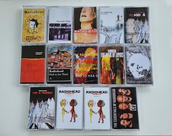 May include: A collection of thirteen Radiohead music cassette tapes arranged in three rows. The albums include Pablo Honey, My Iron Lung, The Bends, OK Computer, Kid A, Amnesiac, Hail to the Thief, In Rainbows, The King of Limbs, A Moon Shaped Pool, Kid A Mnesia, The Best Of, and The Essentials of Radiohead.