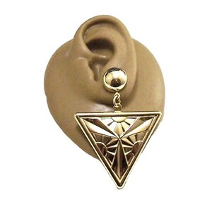 May include: A gold-colored earring with a geometric triangular pendant. The pendant features a sunburst design with intricate details. The earring is attached to a small, round stud.