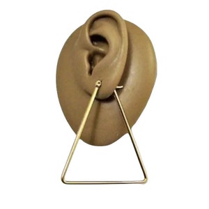 May include: Gold triangle hoop earrings. The earrings are simple and modern, with a minimalist design.