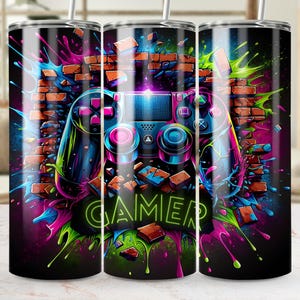 Puede incluir: Un vaso negro con un diseño vibrante que presenta un mando de videojuegos, una pared de ladrillos y el texto verde neón "GAMER". El diseño incorpora salpicaduras de rosa, azul y verde.