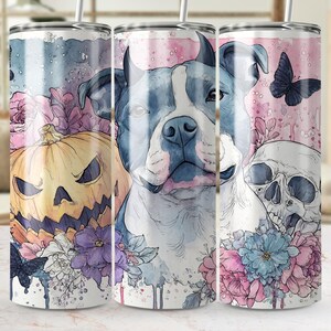 May include: A stainless steel tumbler featuring a watercolor design with a blue and white dog, a jack-o'-lantern, a skull, and flowers. The design includes a butterfly and is set against a pink and blue background.