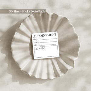 May include: A white sticky note pad with the word "APPOINTMENT" printed at the top, with lines for date, time, and where, and a box for notes and details. The note pad is on a white, textured, decorative plate. The text "50 Sheet Sticky Note Pads" is at the top.