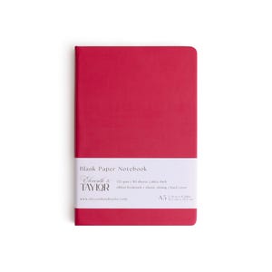 May include: A red A5 notebook with a white band featuring the text "Blank Paper Notebook" and the brand "Eleventh & Co. TAYLOR". The notebook has a hard cover and a ribbon bookmark.