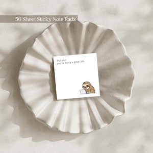 May include: A white sticky note pad with the text "hey you! you're doing a great job." and a cartoon sloth using a laptop. The note pad is on a white, ruffled, ceramic dish. The words "50 Sheet Sticky Note Pads" are at the top.