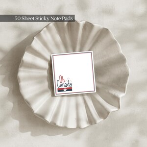 May include: A square sticky note pad with 50 sheets, featuring a white background, a thin red and blue border, and the text Oh Canada in blue with a small white maple leaf icon and red accents at the bottom left corner of each individual sheet.