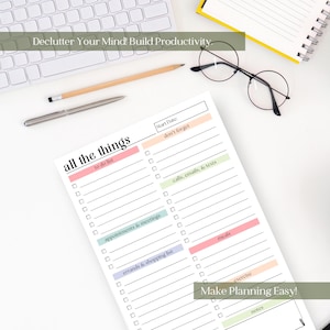 May include: A white notepad with the text "all the things" and sections for to-do lists, appointments, and errands. The notepad is on a white surface with a keyboard, pen, pencil, and glasses. Text on the notepad includes "Make Planning Easy!"