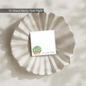 May include: A square sticky note pad with 50 sheets, featuring a white background, a thin black border, and a watercolour illustration of a green succulent in a terracotta pot. The text it's grow time is printed in black in the bottom right corner.