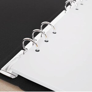 May include: Close-up of an open binder with white paper and silver metal rings. The binder has a black cover and a silver metal clasp. The paper is clean and crisp, and the rings are shiny.