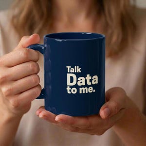 May include: A dark navy blue ceramic mug featuring the white printed text Talk Data to me. The mug has a smooth cylindrical body and a curved handle on the side, providing a simple and functional design for holding hot or cold beverages.