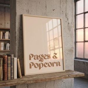 Könnte beinhalten: Ein gerahmter Druck mit den Worten "Pages & Popcorn" in einer braunen Retro-Schriftart. Der Druck zeigt auch Illustrationen eines Bücherstapels und eines Popcornbehälters. Der Druck wird auf einem Holzregal mit einer Büchersammlung ausgestellt.