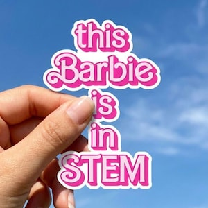 May include: A die-cut vinyl sticker featuring the text "this Barbie is in STEM" written in a bold, retro-style pink font with a white outline. The lettering is stacked in four lines, with the word STEM appearing in all capital letters.
