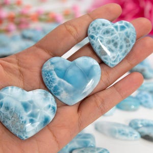 Puede incluir: Tres piedras pulidas en forma de corazón azul y blanco hechas de jaspe oceánico. Las piedras están en la palma de una mano.