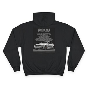 Puede incluir: Sudadera con capucha negra con un gráfico de BMW M3. El gráfico incluye la imagen y las especificaciones del coche. La sudadera está hecha de un material suave y tiene un diseño clásico.