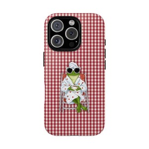 May include: A red and white gingham patterned phone case featuring a cartoon frog wearing sunglasses, a robe, and a towel on its head. The frog is sitting in a beach chair and holding a cup of coffee.