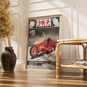 May include: Framed poster featuring the anime film "Akira." The artwork showcases a red motorcycle with the word "Canon" on it, set against a black and white background. The poster is displayed in a room with a vase of dried plants.