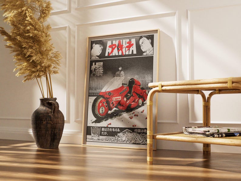 May include: Framed poster featuring the anime film "Akira." The artwork showcases a red motorcycle with the word "Canon" on it, set against a black and white background. The poster is displayed in a room with a vase of dried plants.