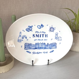 Può includere: Piatto ovale in ceramica bianca con illustrazioni e testo blu. Il piatto presenta un disegno di un edificio, calici di champagne, una palla da discoteca e un cane. Il testo include "Mr & Mrs SMITH 29th March 2024" e "Hawlstone Hall".