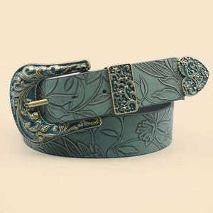 Könnte beinhalten: Ein teal-farbener Gürtel mit floralem Muster und dekorativer Schnalle. Die Schnalle und das Endstück sind mit teal- und goldfarbenen Details versehen. Der Gürtel besteht aus einem strukturierten Material und ist etwa 3 cm breit.