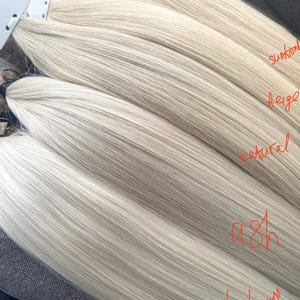 May include: A selection of blonde hair extensions, with shades labelled 'sun-kissed', 'beige', 'natural', 'ash', and 'platinum'. The hair appears straight and smooth. The image displays a range of colours for hair extensions.