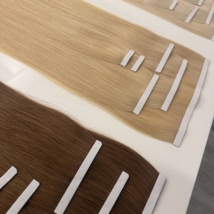 Puede incluir: Tres paquetes de extensiones de cabello en tonos rubios y marrones. Cada paquete tiene tiras adhesivas para una fácil aplicación. El cabello es liso y brillante, dispuesto sobre una superficie blanca.