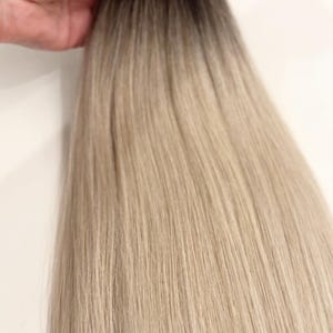 Op de afbeelding: Een bundel hairextensions met een donkerbruine aanzet die overgaat in een lichtblonde tint. Het haar wordt bij elkaar gehouden door een zwarte band.