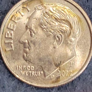 May include: A close-up of a United States dime coin. The coin features a profile of a man, the word "LIBERTY" at the top, and the words "IN GOD WE TRUST" at the bottom. The year "2022" is visible.