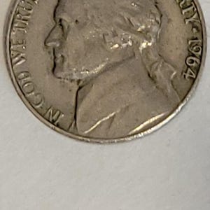 May include: A silver 1964 Jefferson nickel. The obverse features a profile of Thomas Jefferson, the words "LIBERTY" and "IN GOD WE TRUST", and the date. The coin is slightly worn.