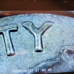 May include: Close-up of a silver coin with the letters "TY" visible. The coin's surface has a textured appearance. The date and time "2026/02/27 21:40:49" are at the bottom of the image.