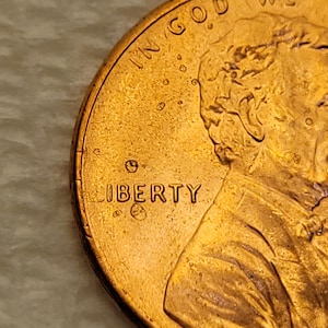 May include: Close-up of a copper-colored penny. The word "LIBERTY" is visible, along with the year and other details. The coin has a worn appearance, with visible scratches and imperfections.