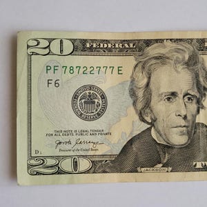 May include: A twenty-dollar bill featuring a portrait of Andrew Jackson on the right side. The note displays the text FEDERAL RESERVE SYSTEM, the serial number PF 78722777 E, and the words THIS NOTE IS LEGAL TENDER FOR ALL DEBTS, PUBLIC AND PRIVATE.