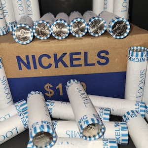 May include: A box of nickels with the word "NICKELS" printed in large blue letters. Rolls of nickels are scattered around the box, with the ends of the rolls showing the coins. The rolls are wrapped in white paper with blue stripes and the text "LOOMIS".