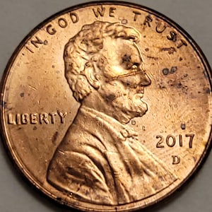 May include: A close-up of a copper-colored 2017 United States penny. The coin features the profile of Abraham Lincoln, the word "LIBERTY", and the phrase "IN GOD WE TRUST". The year "2017" is visible.